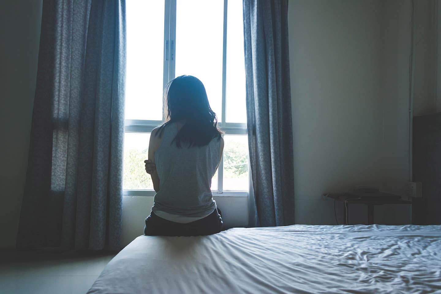 Woman sitting on edge of bed looking out window